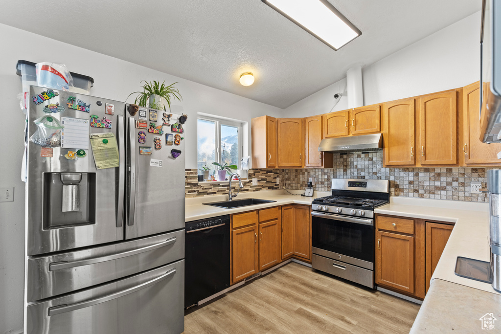 Kitchen featuring tasteful backsplash, stainless steel appliances, sink, vaulted ceiling, and light hardwood / wood-style floors