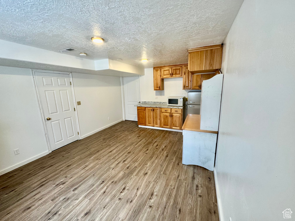Kitchen with light countertops, visible vents, white microwave, brown cabinetry, and wood finished floors