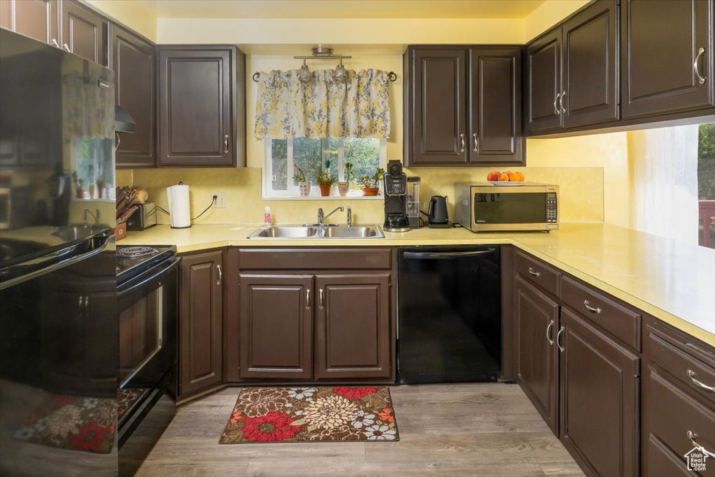 Kitchen with black appliances, dark brown cabinets, sink, and light hardwood / wood-style floors