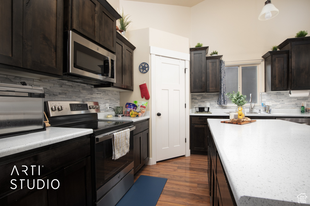 Kitchen with sink, appliances with stainless steel finishes, dark hardwood / wood-style flooring, and decorative backsplash