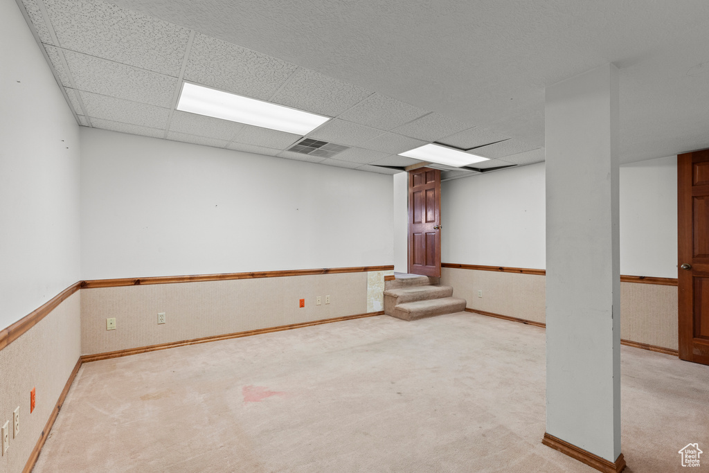 Spare room featuring baseboards, light colored carpet, and a drop ceiling