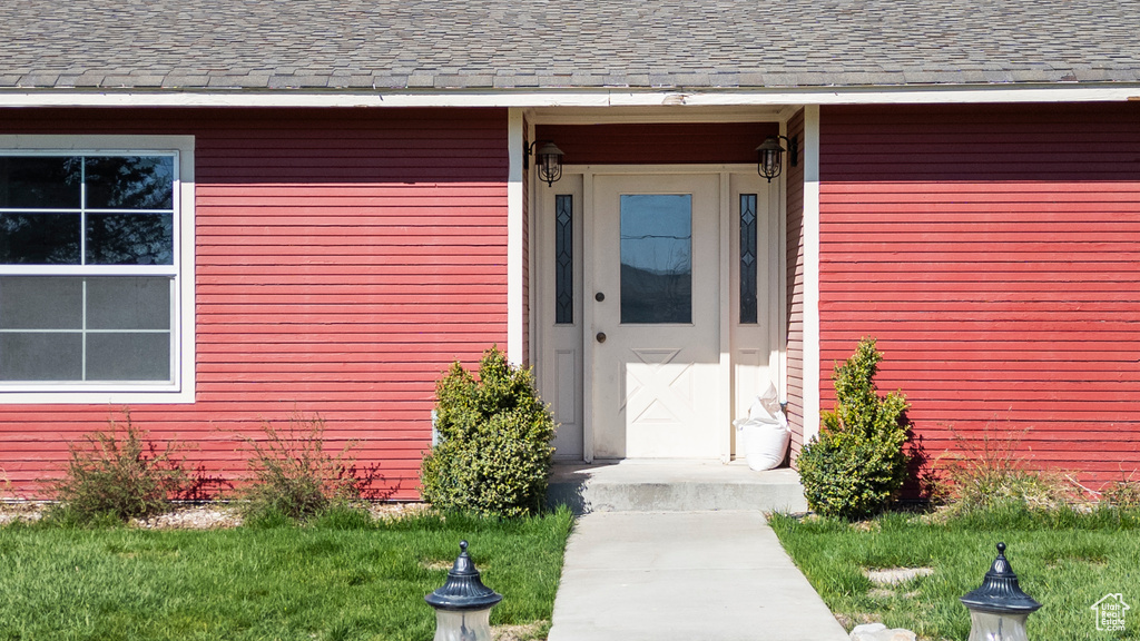 Doorway to property with a shingled roof and a lawn