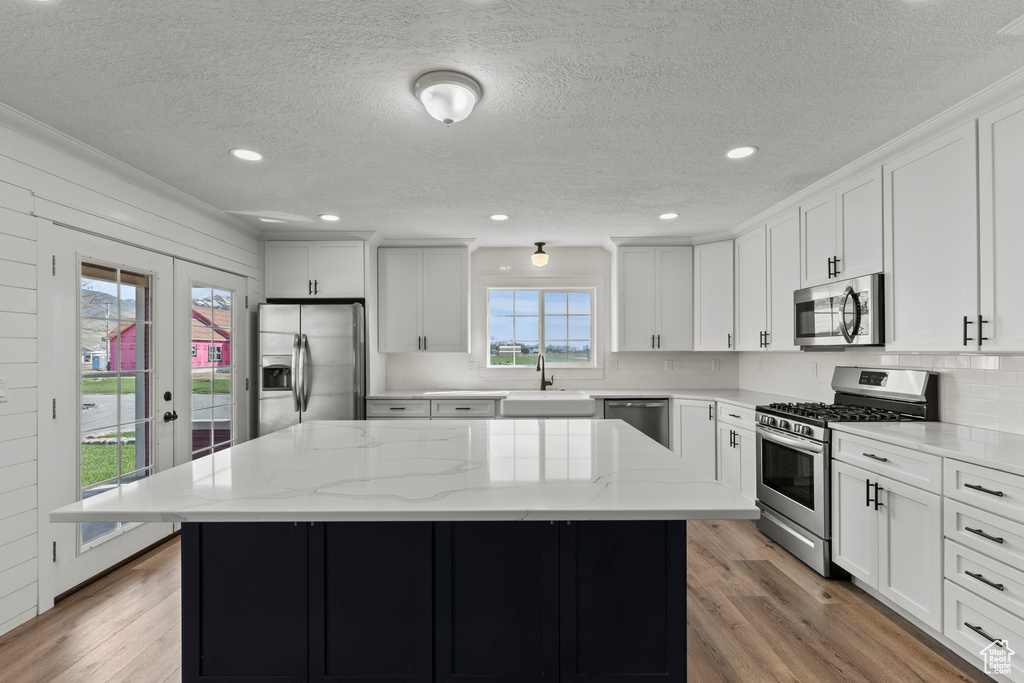 Kitchen featuring stainless steel appliances, a sink, a textured ceiling, a kitchen island, and light wood-type flooring