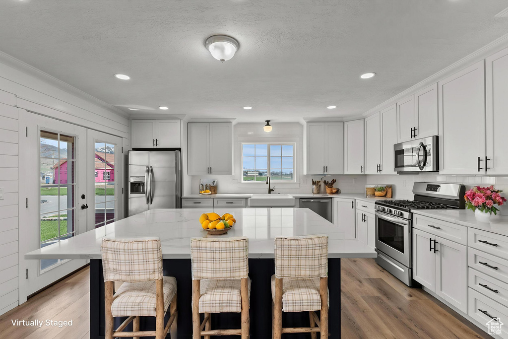 Kitchen featuring stainless steel appliances, a sink, a kitchen breakfast bar, light wood-type flooring, and recessed lighting