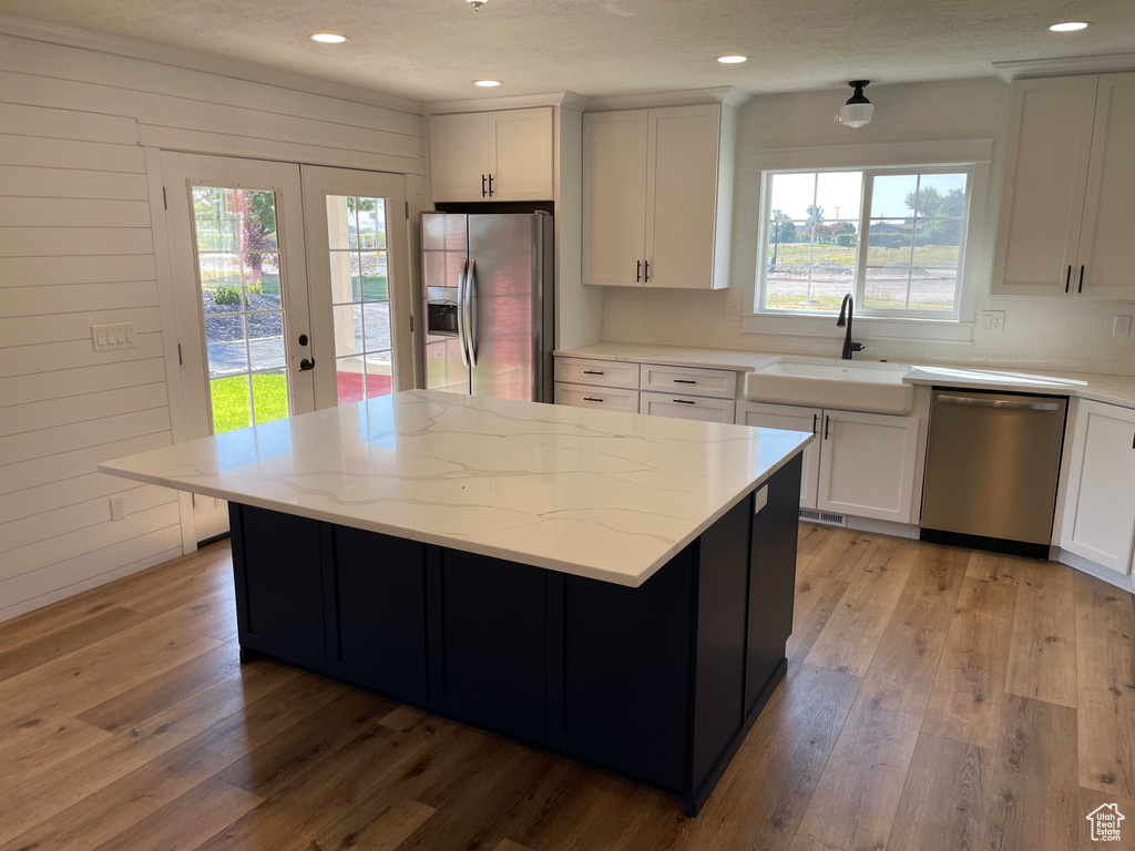 Kitchen with light hardwood / wood-style flooring, appliances with stainless steel finishes, white cabinetry, and a healthy amount of sunlight