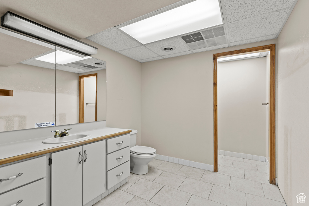 Bathroom featuring vanity, toilet, tile patterned flooring, a drop ceiling, and baseboards