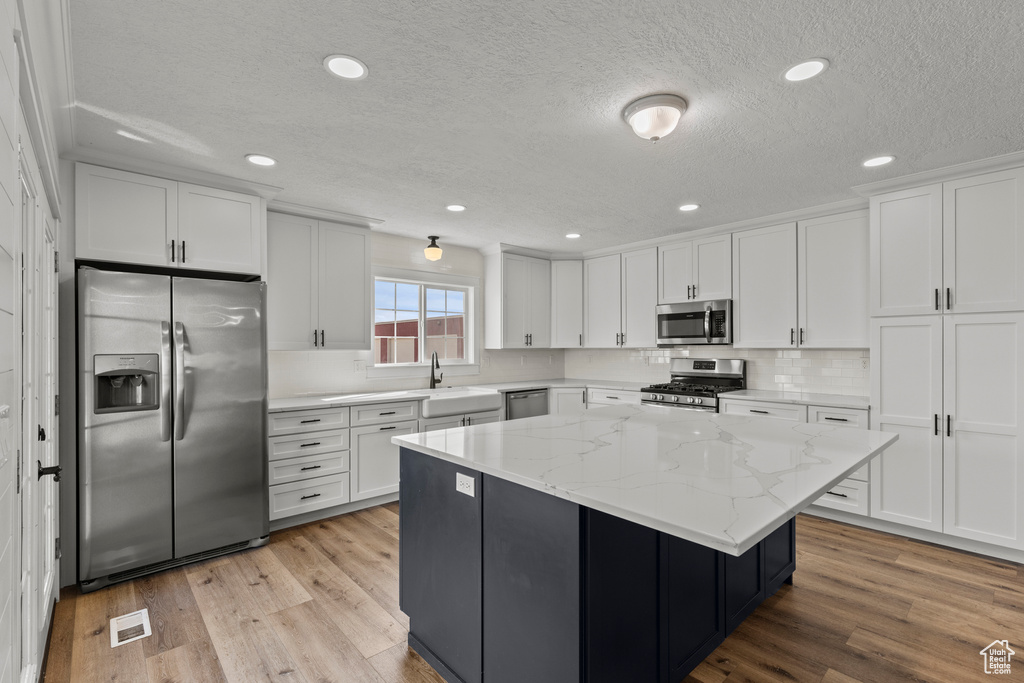 Kitchen with appliances with stainless steel finishes, a textured ceiling, white cabinetry, a center island, and light wood-type flooring