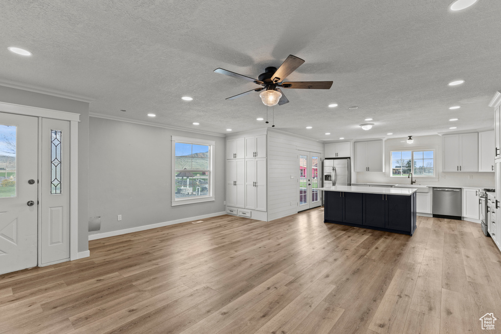 Kitchen featuring appliances with stainless steel finishes, white cabinets, a textured ceiling, light wood-style flooring, and ornamental molding