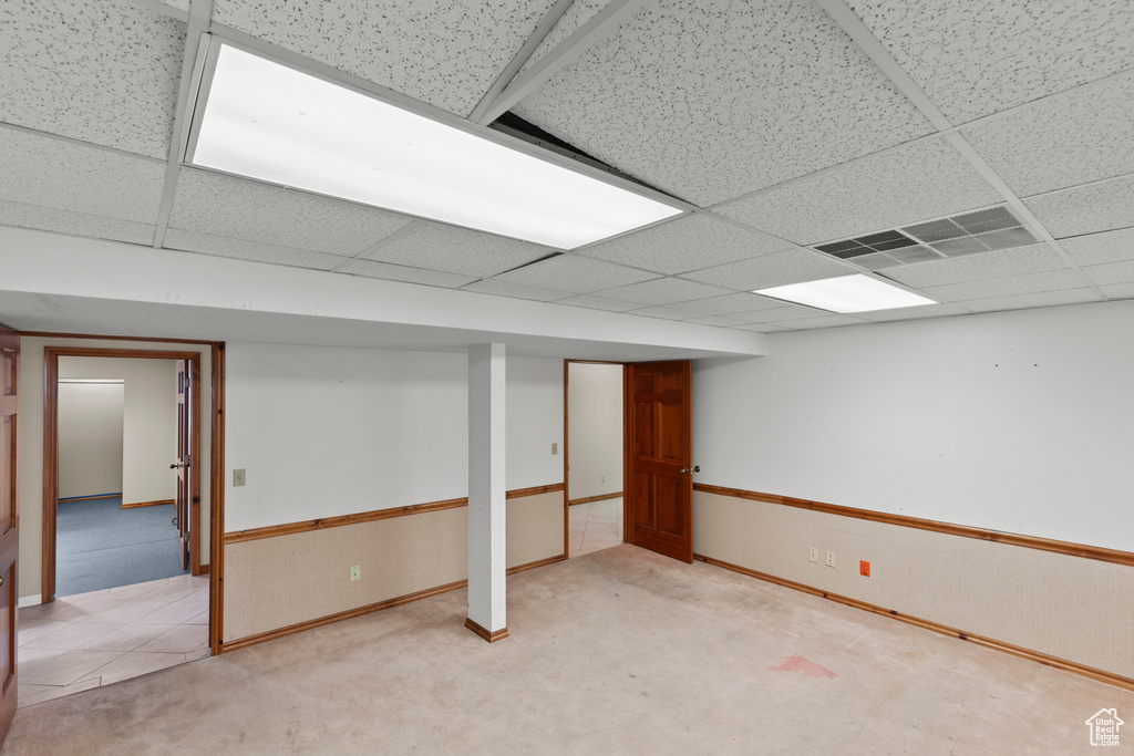 Finished below grade area featuring a paneled ceiling, baseboards, and light carpet