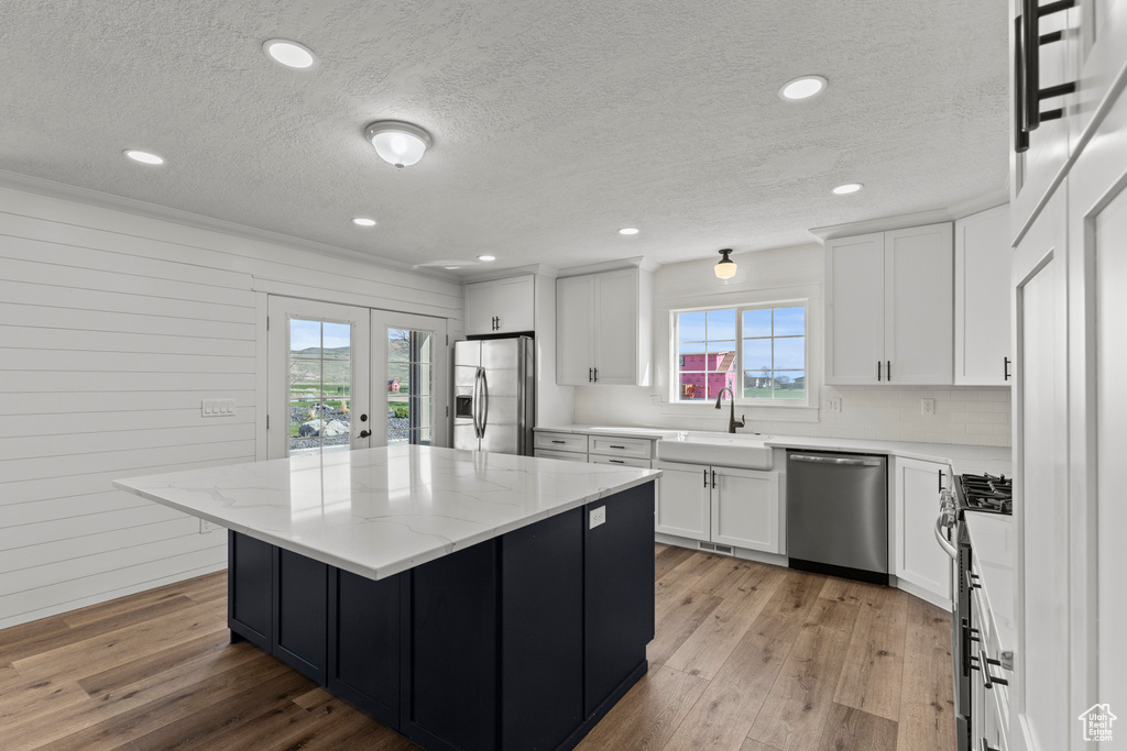 Kitchen with appliances with stainless steel finishes, a sink, plenty of natural light, a textured ceiling, and white cabinetry
