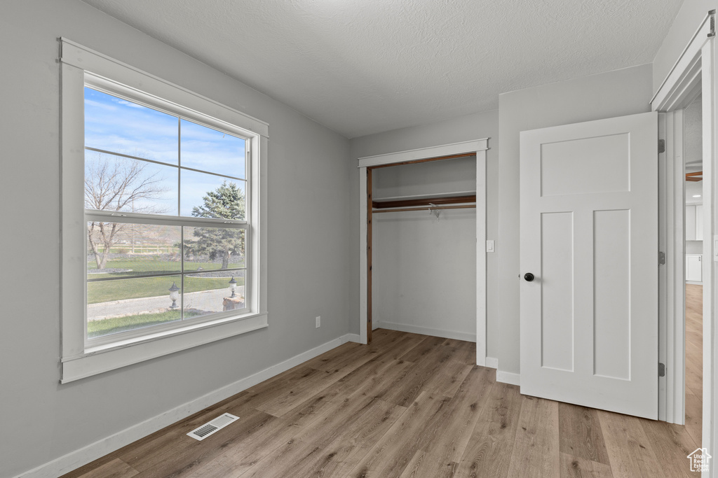 Unfurnished bedroom with light wood finished floors, baseboards, a closet, and a textured ceiling