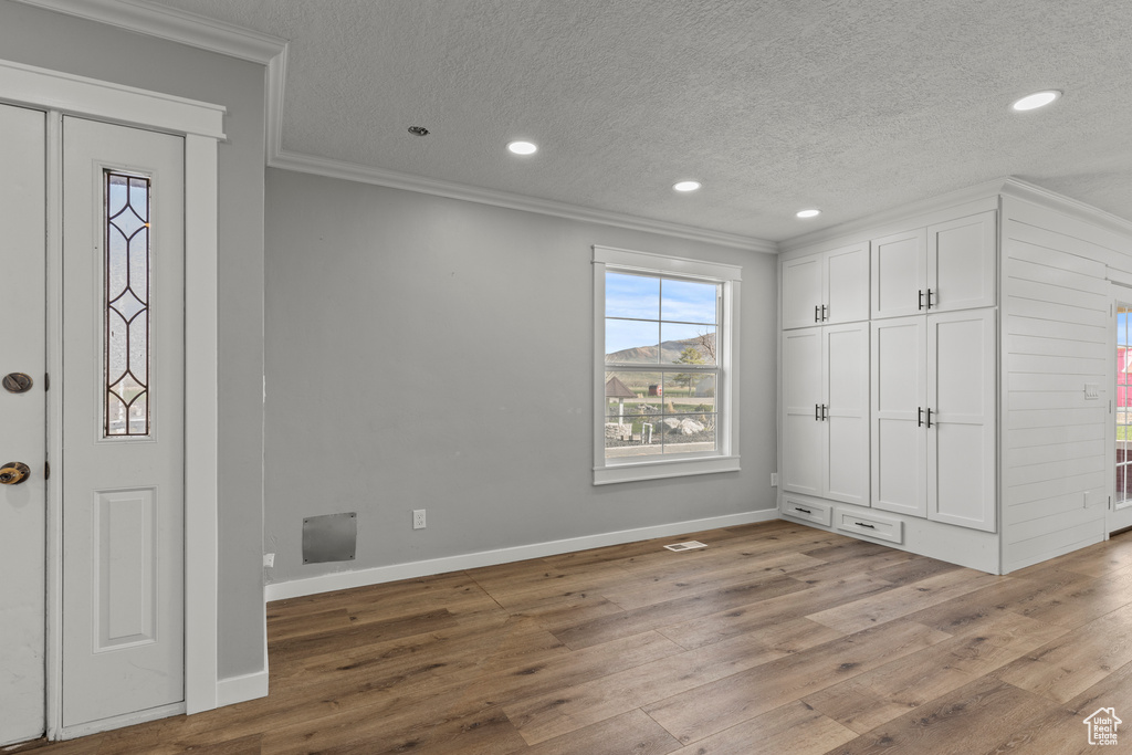 Entrance foyer with crown molding, wood finished floors, a textured ceiling, baseboards, and recessed lighting