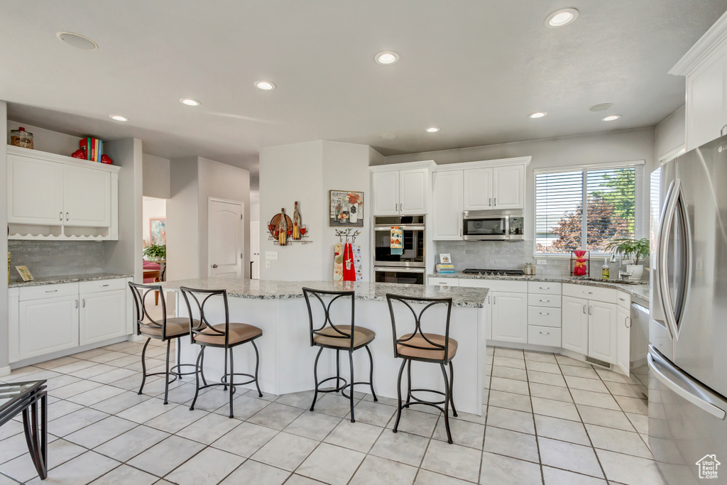 Kitchen featuring light tile patterned floors, white cabinetry, appliances with stainless steel finishes, a center island, and light stone countertops