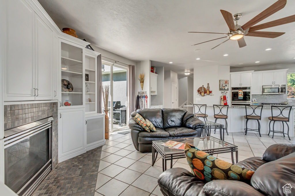 Living room featuring ceiling fan, a fireplace, and light tile patterned floors