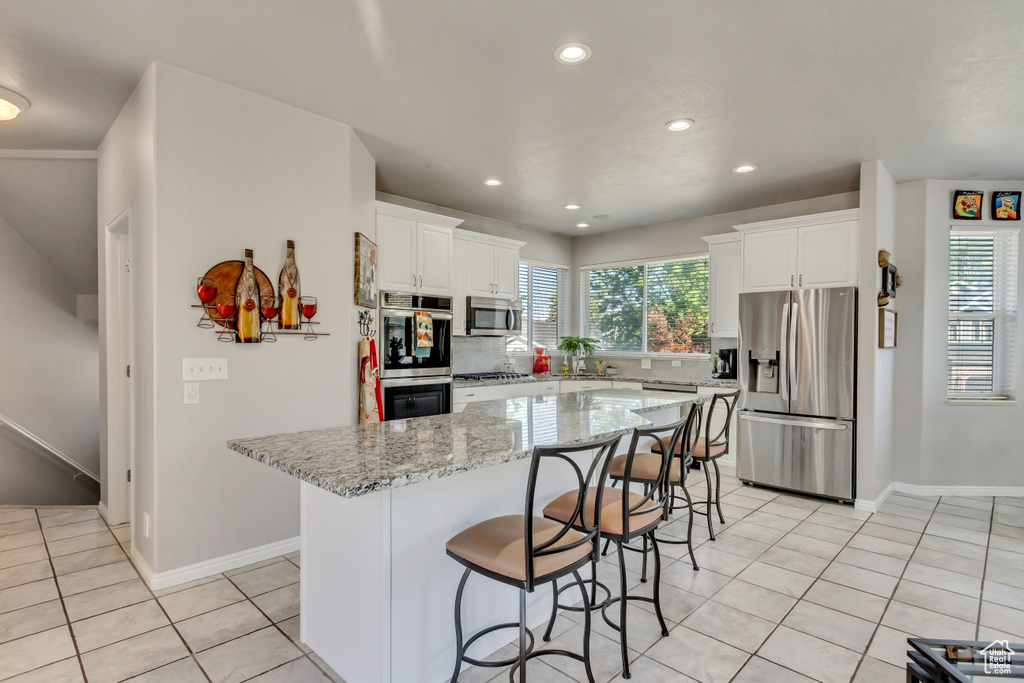 Kitchen featuring tasteful backsplash, light stone counters, appliances with stainless steel finishes, a center island, and white cabinetry