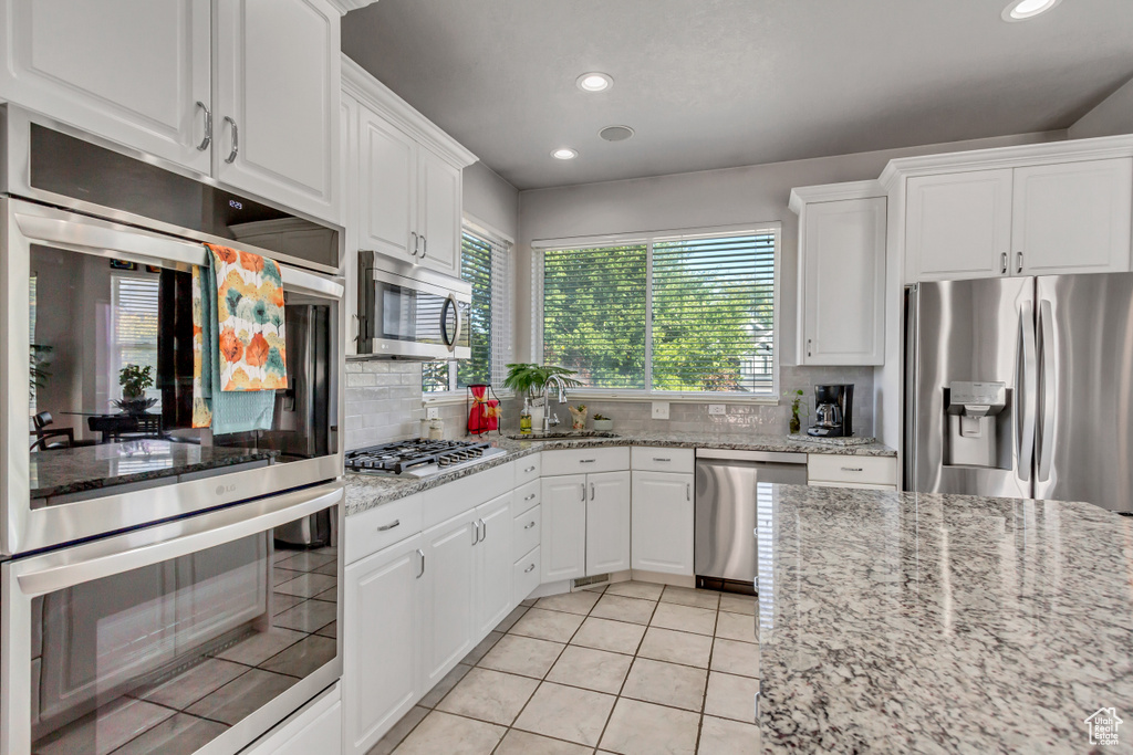 Kitchen with light stone counters, white cabinets, sink, tasteful backsplash, and appliances with stainless steel finishes