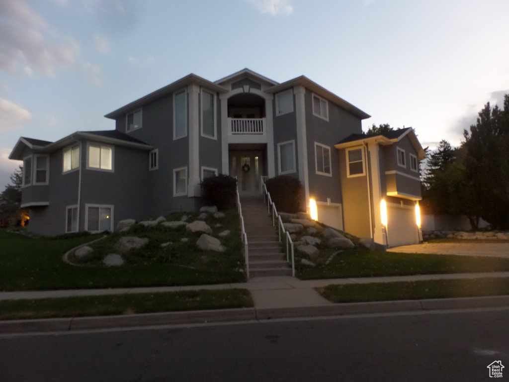 View of front of property featuring a balcony, a lawn, and a garage