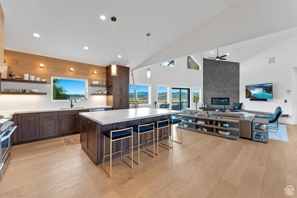 Kitchen featuring a fireplace, light wood-type flooring, ceiling fan, a kitchen island, and a breakfast bar