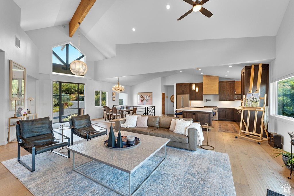 Living room featuring ceiling fan with notable chandelier, high vaulted ceiling, a healthy amount of sunlight, and light hardwood / wood-style floors