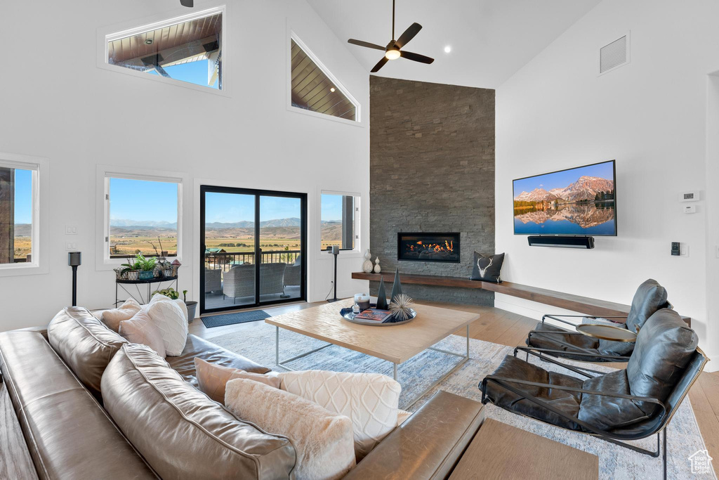 Living room with a fireplace, high vaulted ceiling, light hardwood / wood-style flooring, and ceiling fan