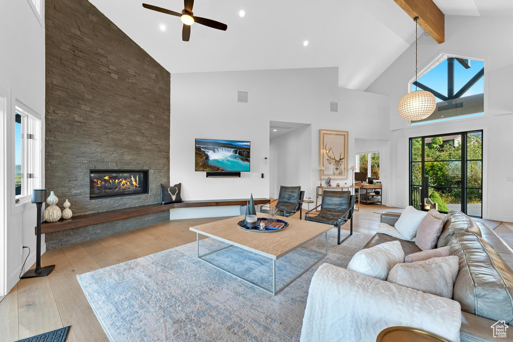 Living room with light wood-type flooring, beamed ceiling, high vaulted ceiling, a large fireplace, and ceiling fan