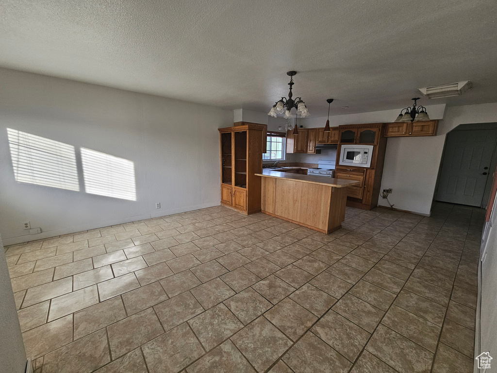 Kitchen featuring white appliances, decorative light fixtures, a textured ceiling, a notable chandelier, and kitchen peninsula