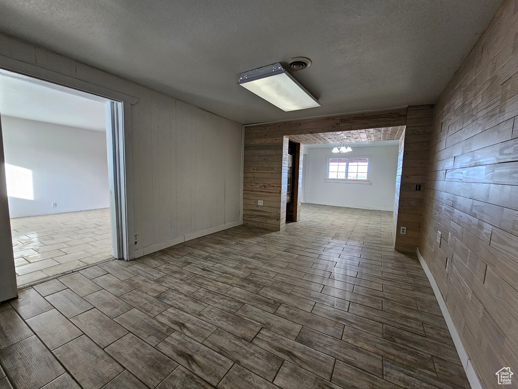 Empty room featuring wooden walls, a textured ceiling, and an inviting chandelier