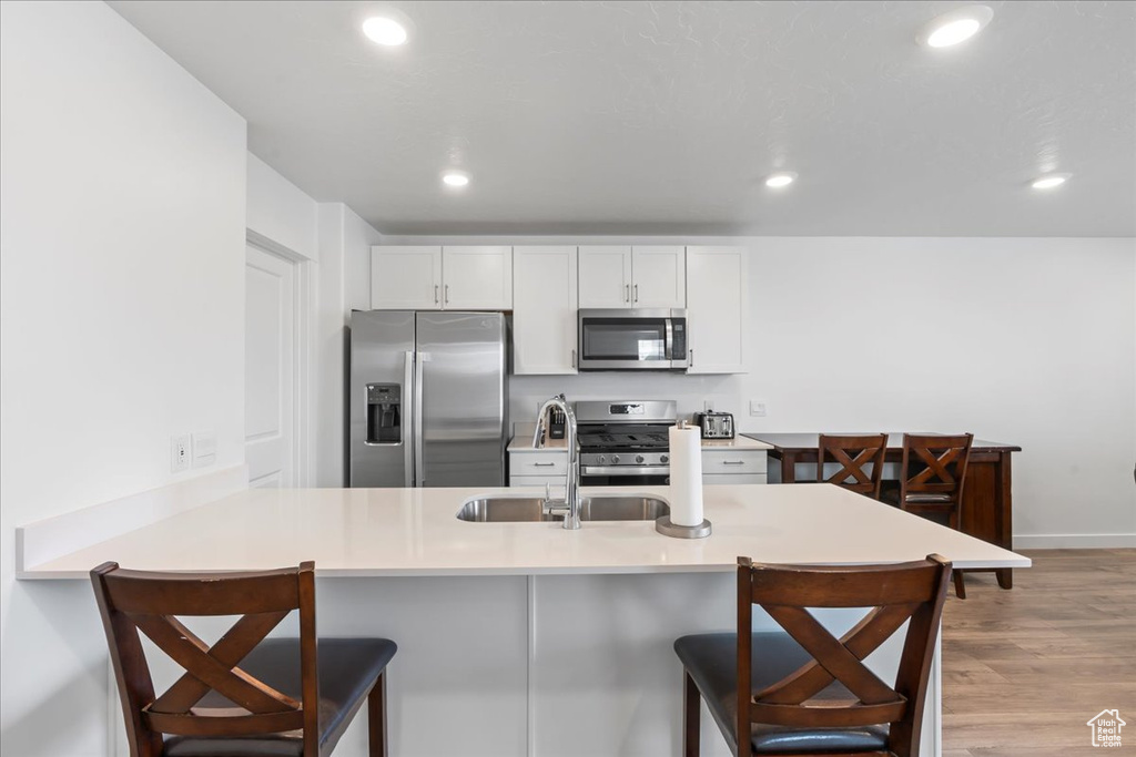 Kitchen featuring a kitchen bar, stainless steel appliances, light wood-type flooring, and white cabinets