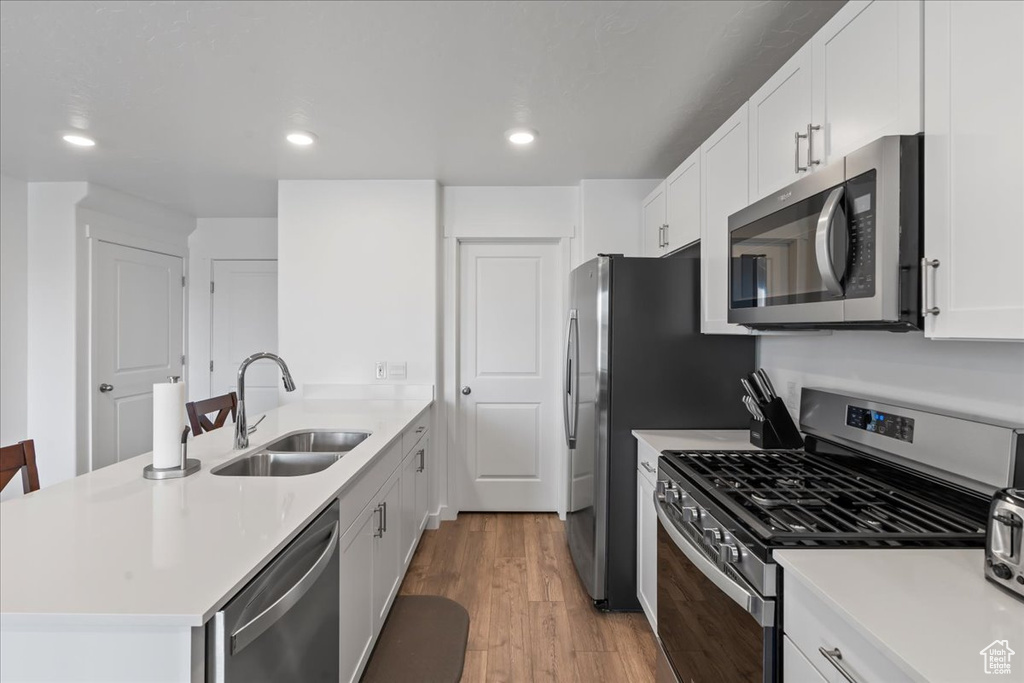 Kitchen featuring light hardwood / wood-style floors, stainless steel appliances, sink, kitchen peninsula, and white cabinetry