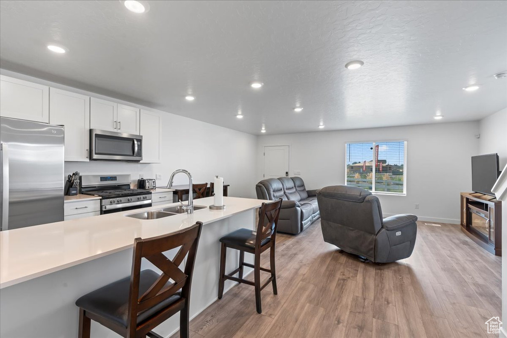 Kitchen featuring appliances with stainless steel finishes, light hardwood / wood-style floors, a kitchen bar, sink, and white cabinetry