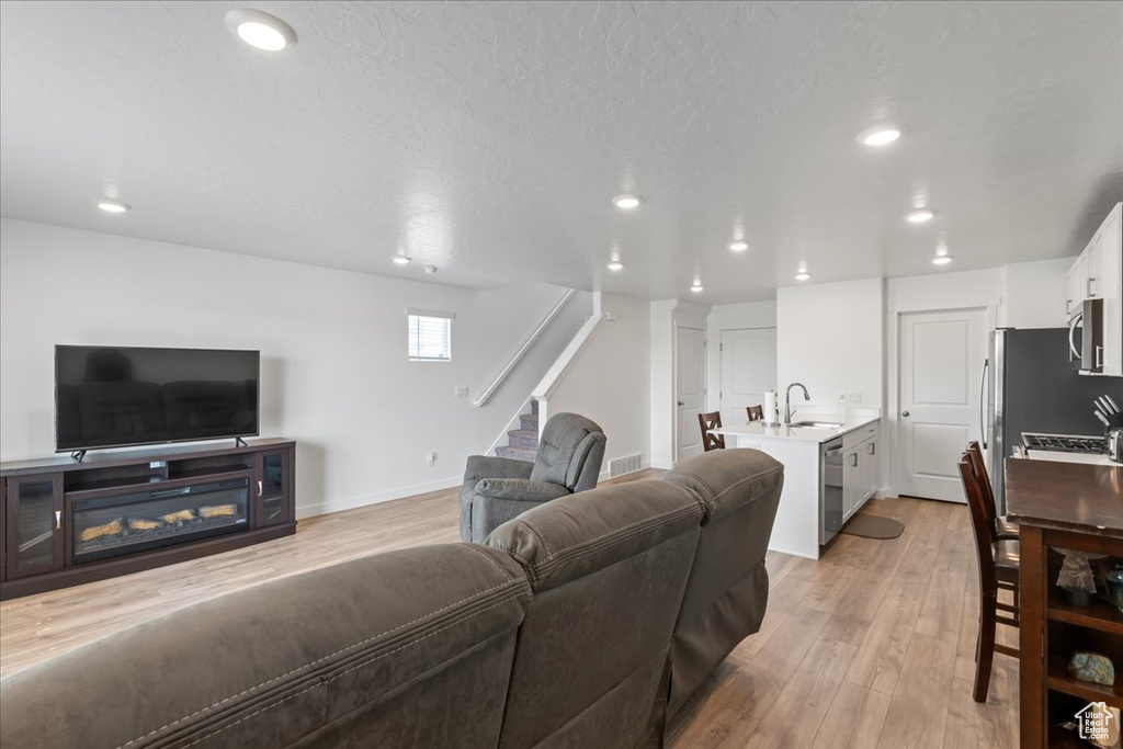 Living room featuring a textured ceiling, sink, and light wood-type flooring