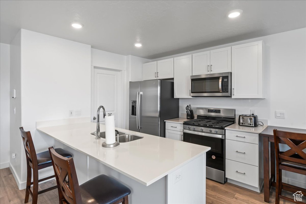 Kitchen with white cabinets, stainless steel appliances, light hardwood / wood-style floors, sink, and a breakfast bar