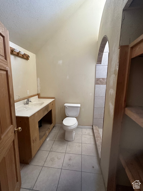 Bathroom with lofted ceiling, tile patterned flooring, toilet, and vanity