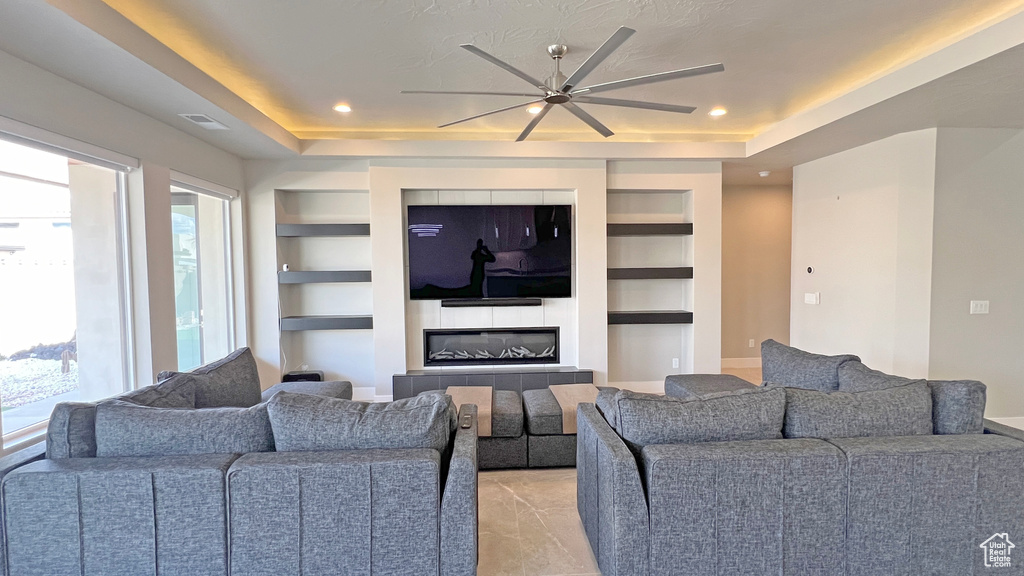 Living room with built in features, a tray ceiling, ceiling fan, and a fireplace