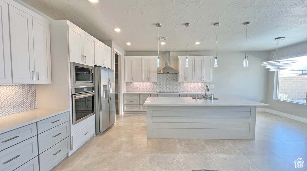 Kitchen with pendant lighting, sink, appliances with stainless steel finishes, a center island with sink, and wall chimney range hood