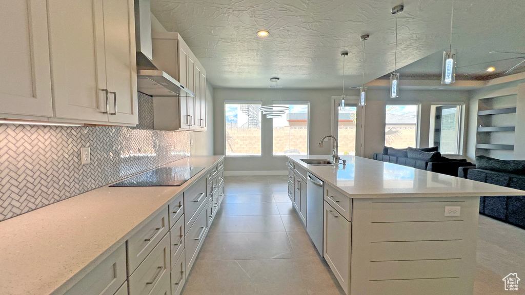 Kitchen featuring sink, wall chimney exhaust hood, light tile patterned flooring, black electric stovetop, and a kitchen island with sink