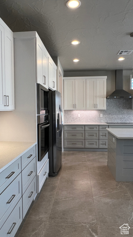 Kitchen featuring backsplash, stainless steel appliances, gray cabinets, wall chimney range hood, and white cabinets