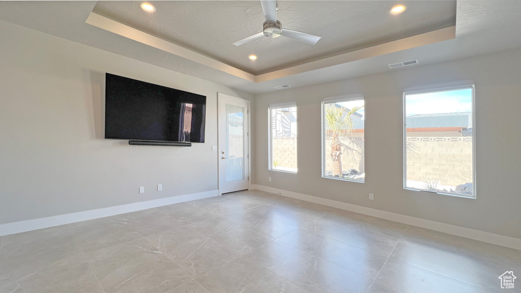 Empty room with ceiling fan and a tray ceiling