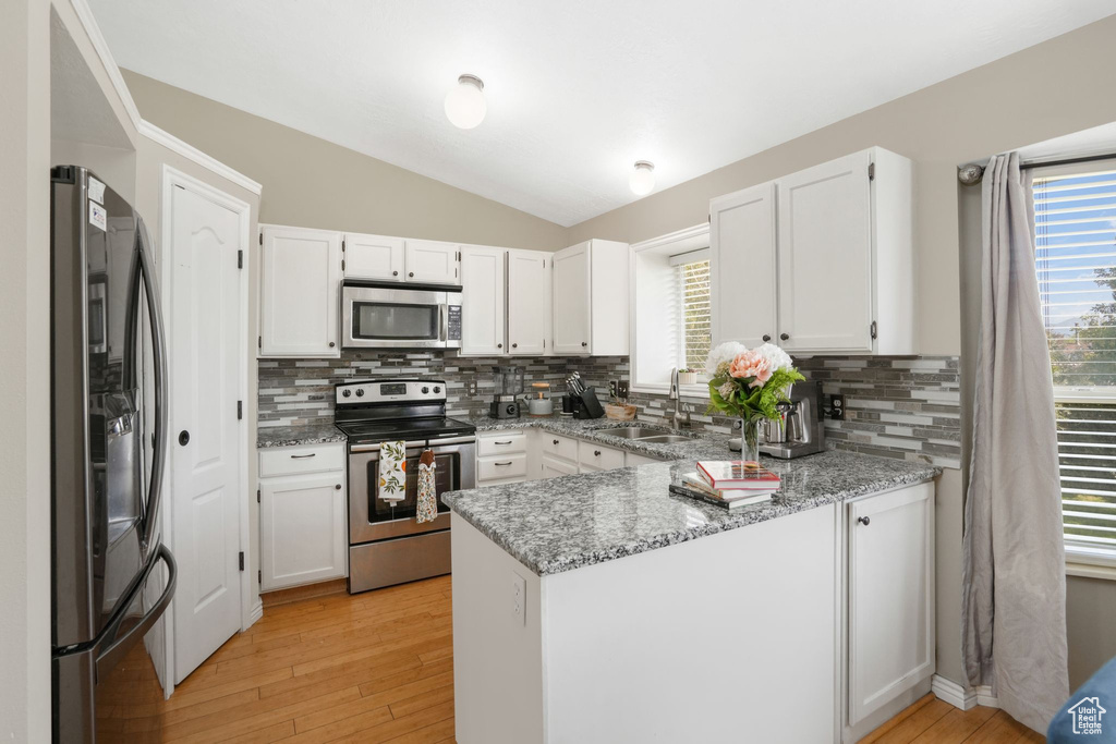 Kitchen featuring kitchen peninsula, appliances with stainless steel finishes, white cabinetry, and light hardwood / wood-style floors