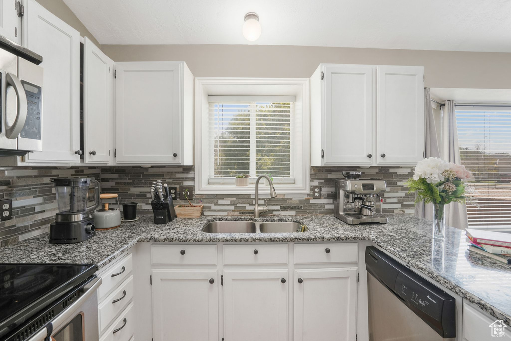 Kitchen featuring light stone countertops, backsplash, appliances with stainless steel finishes, sink, and white cabinetry