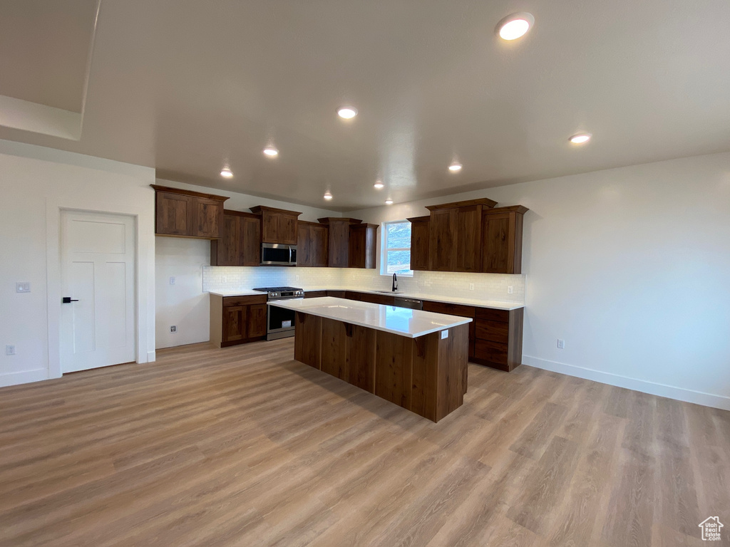 Kitchen featuring backsplash, stainless steel appliances, light hardwood / wood-style floors, sink, and a kitchen island