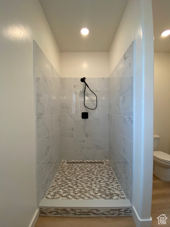 Bathroom with tiled shower, wood-type flooring, and toilet