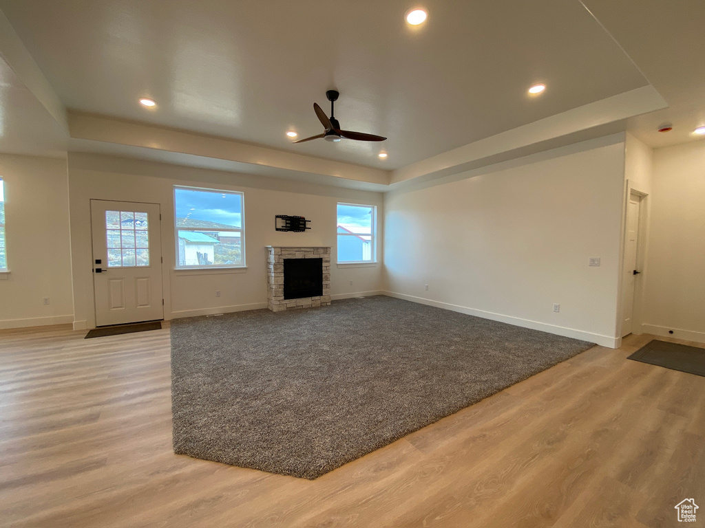 Unfurnished living room featuring a tray ceiling, ceiling fan, a fireplace, and light hardwood / wood-style flooring