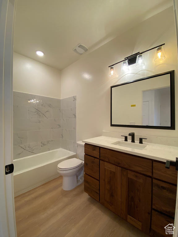 Full bathroom with hardwood / wood-style floors, tiled shower / bath, toilet, and vanity