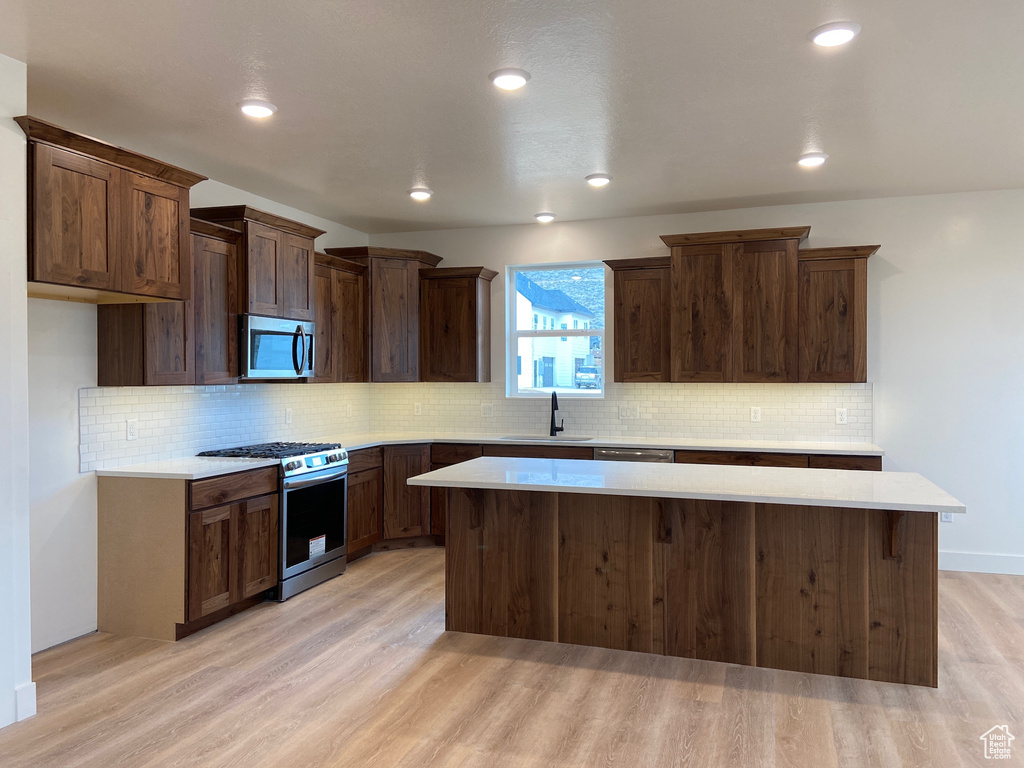 Kitchen with appliances with stainless steel finishes, a center island, light hardwood / wood-style floors, and sink