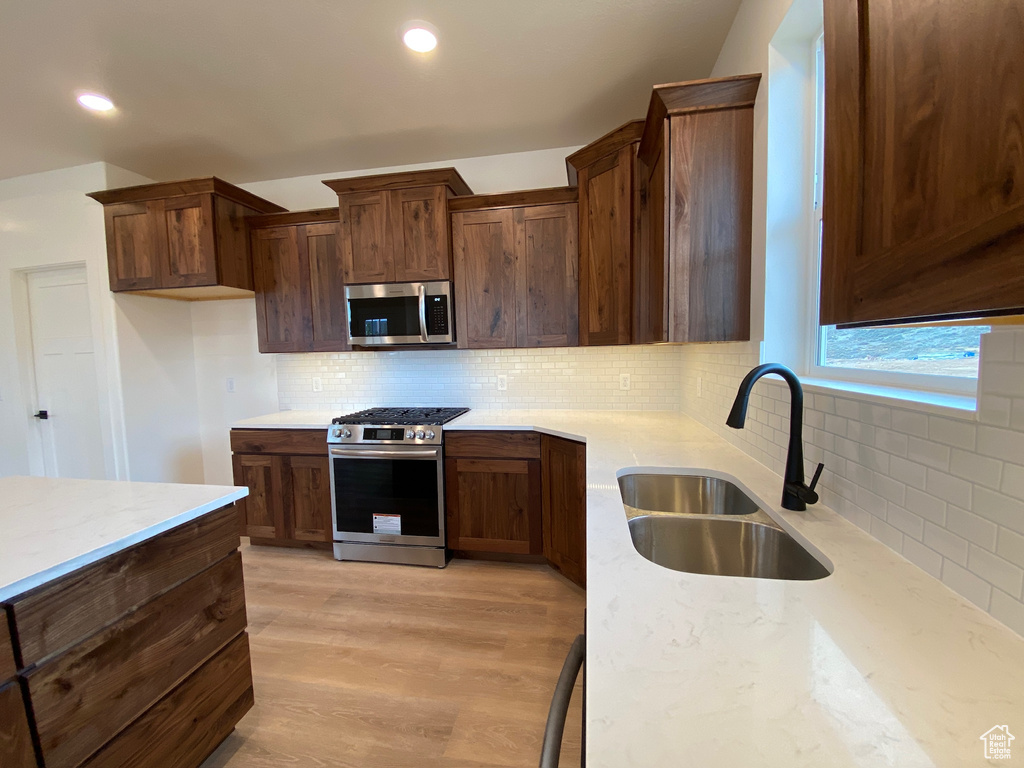 Kitchen featuring light stone countertops, stainless steel appliances, sink, decorative backsplash, and light wood-type flooring