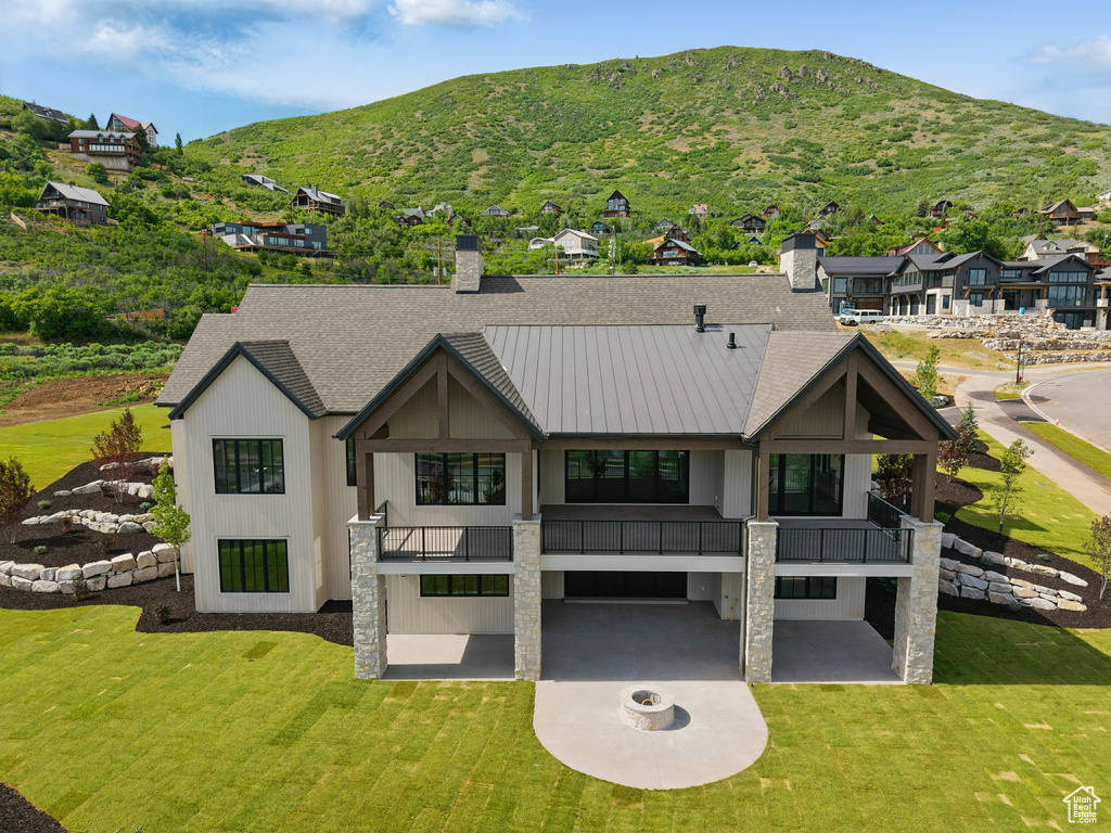 Back of house featuring a balcony, a chimney, a mountain view, and a yard