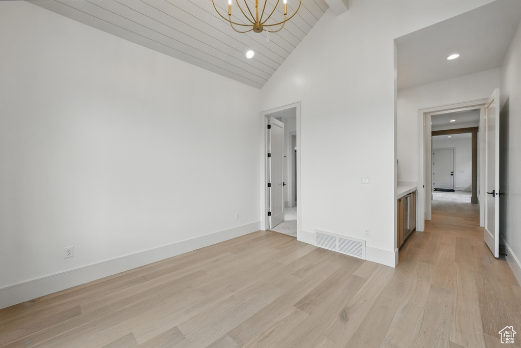 Unfurnished room featuring a chandelier, light wood-type flooring, recessed lighting, baseboards, and beam ceiling