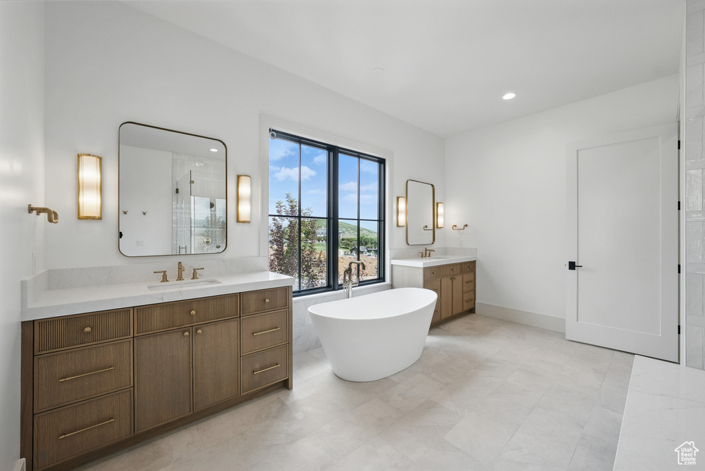Bathroom with two vanities, a freestanding tub, walk in shower, and recessed lighting