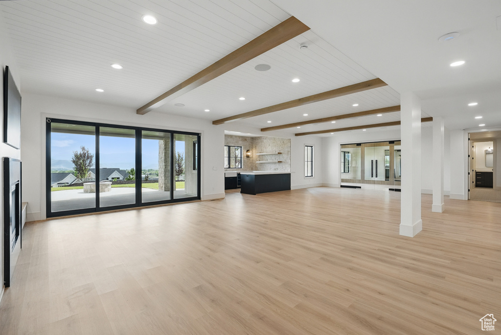 Unfurnished living room featuring recessed lighting, baseboards, light wood finished floors, beamed ceiling, and healthy amount of natural light